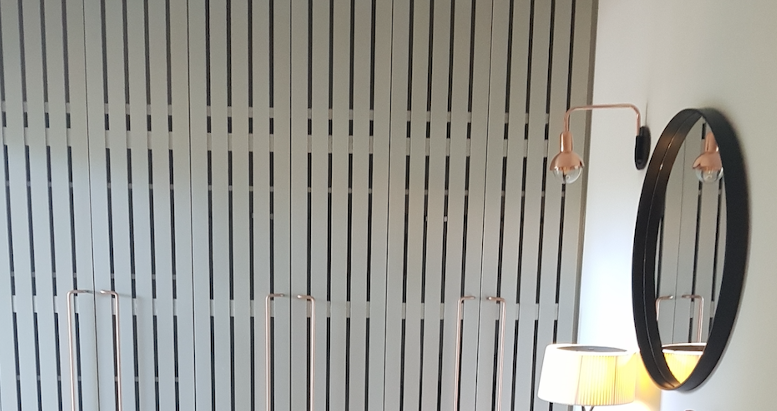 Slatted wardrobe doors with copper handles beside a round black mirror and copper wall light