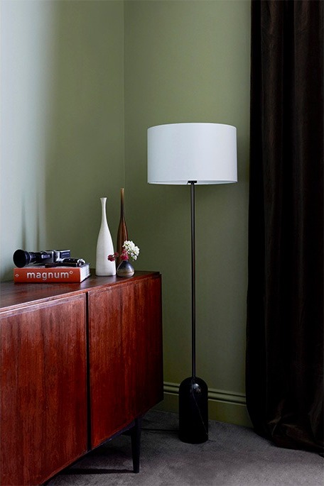Teak sideboard and floor lamp against a sage green wall