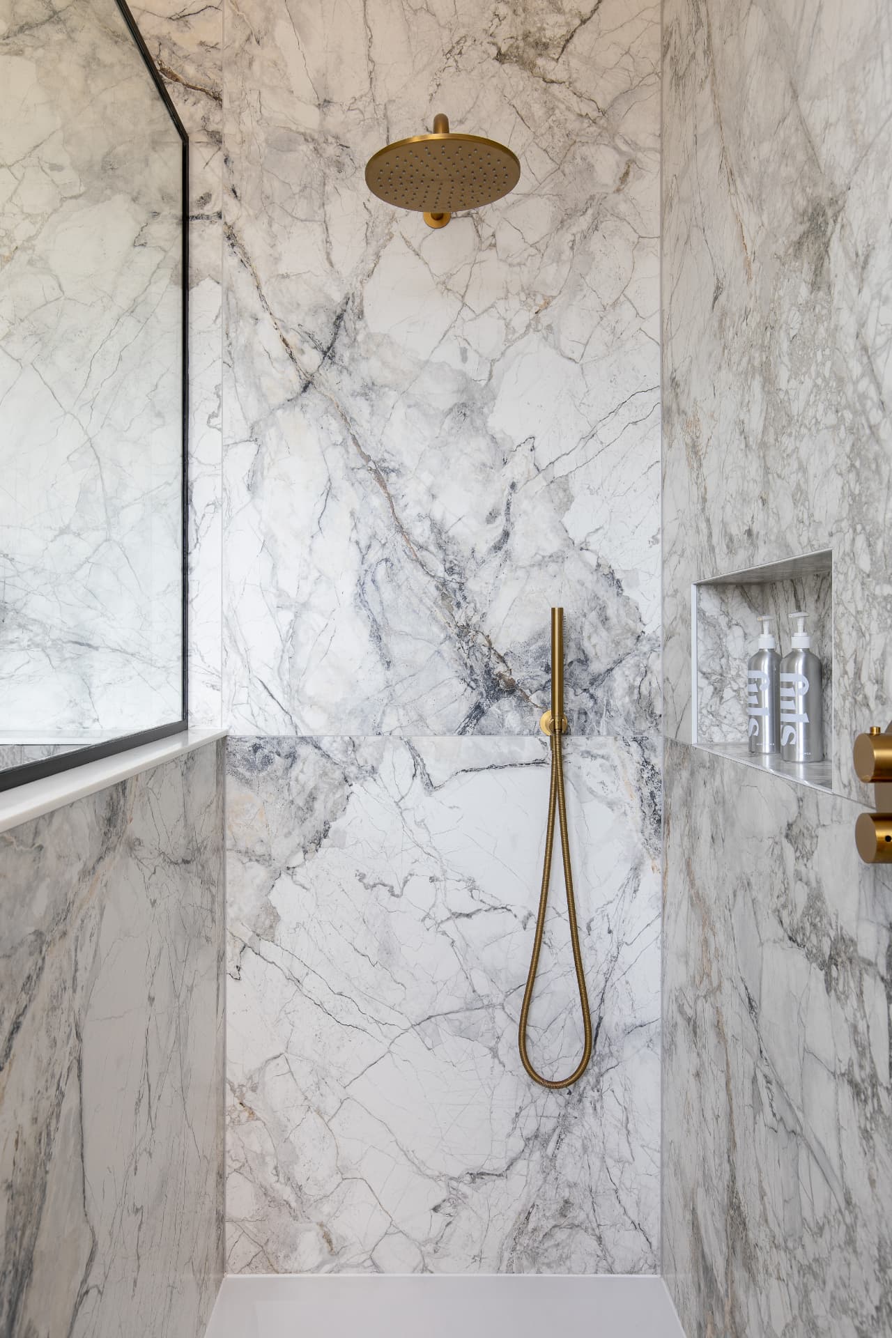 Walk-in shower in Crystal Palace with a brushed brass rainfall head, handheld wand, recessed niche and marble-effect walls