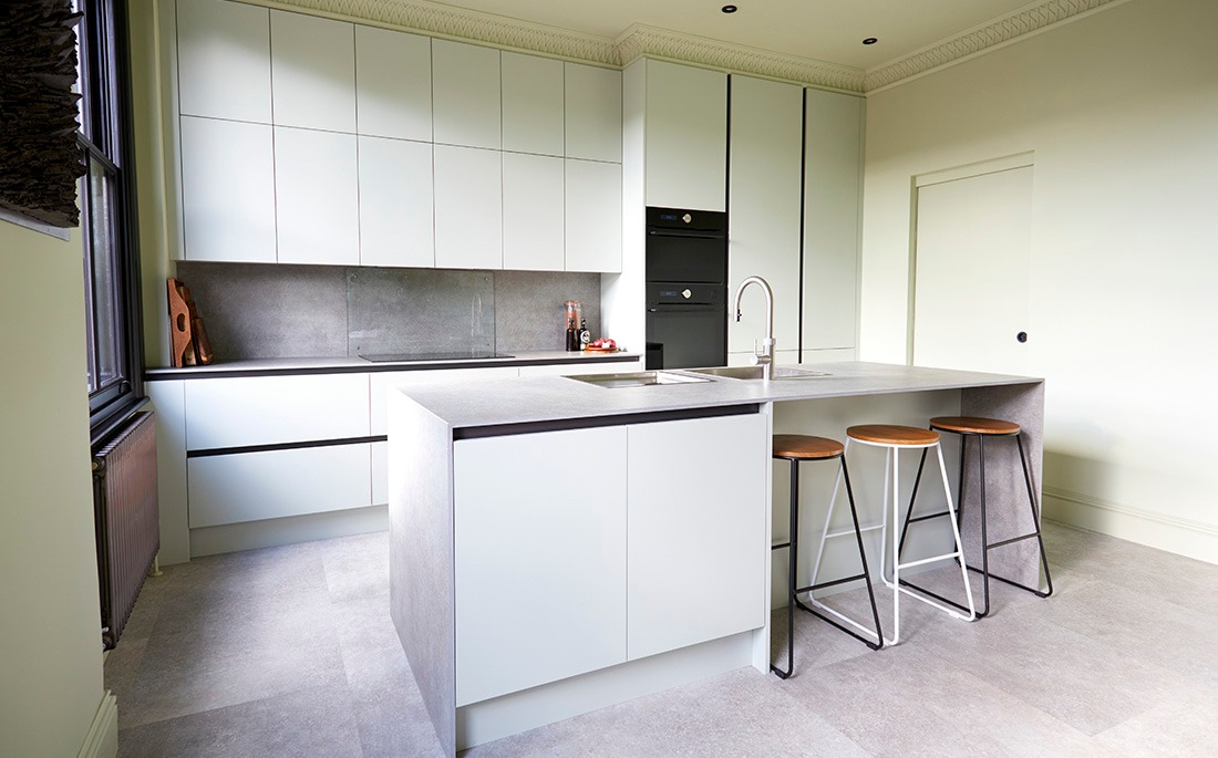 Pale grey handleless kitchen with stone worktops, integrated ovens and bar stools