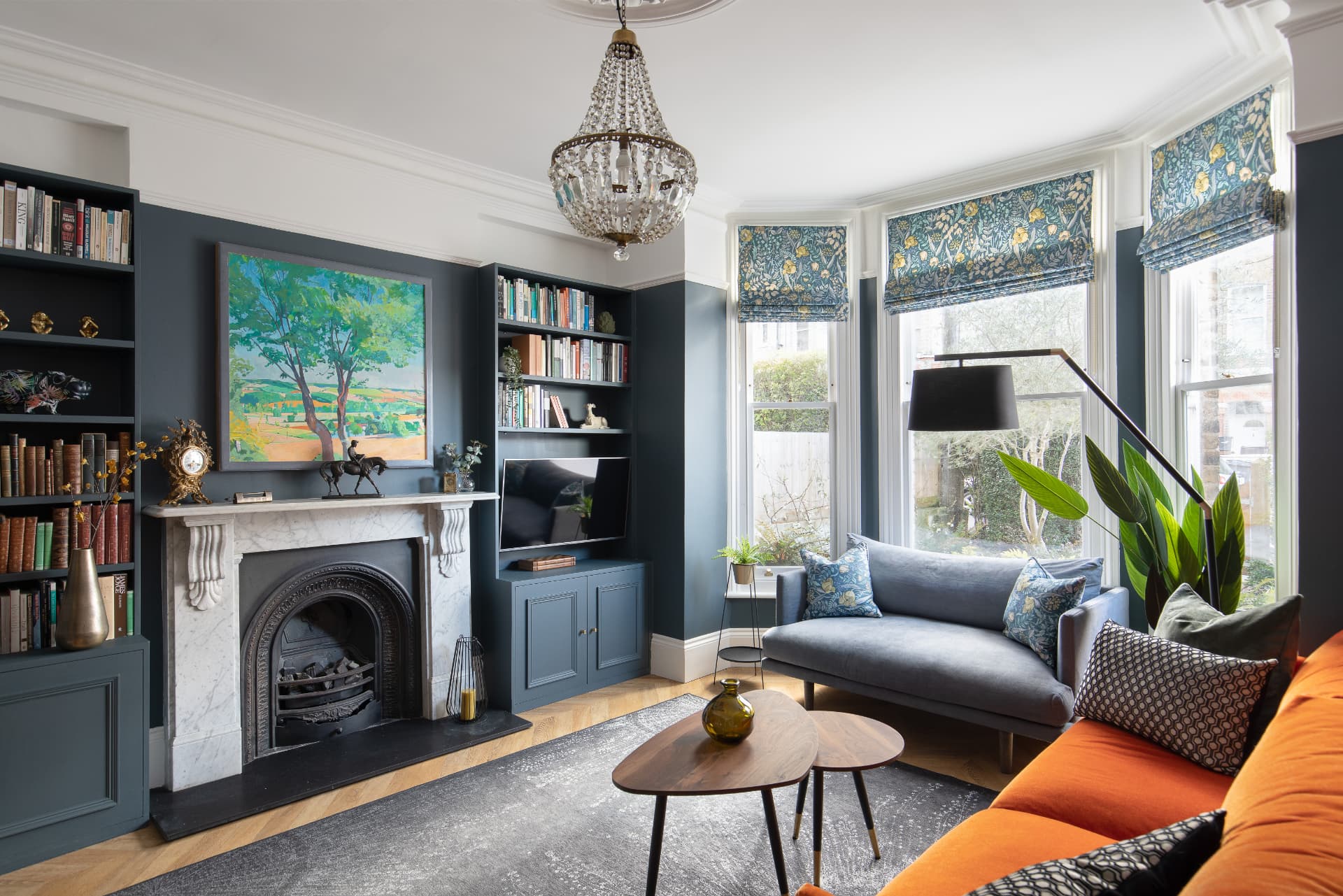 Deep blue Victorian living room in Crystal Palace with marble fireplace, bay window, built-in bookshelves and orange velvet sofa