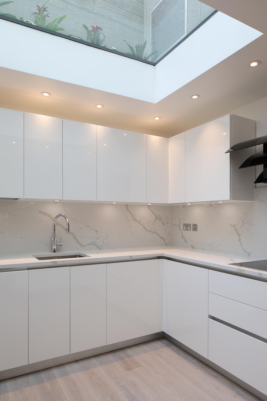 High-gloss white kitchen with marble-effect splashback beneath a large roof window