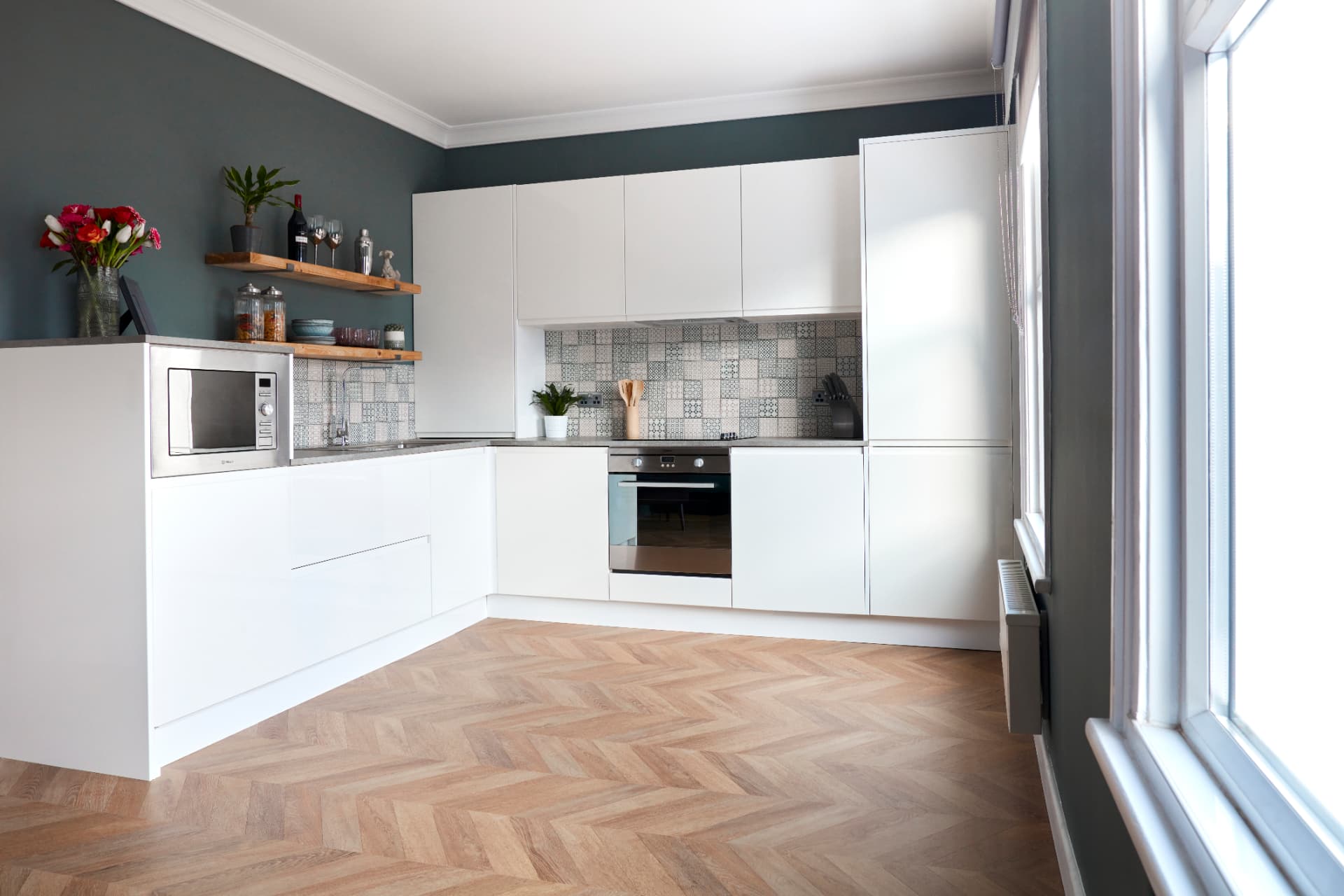 White handleless L-shaped kitchen with herringbone floor, patterned tiles and open wooden shelves