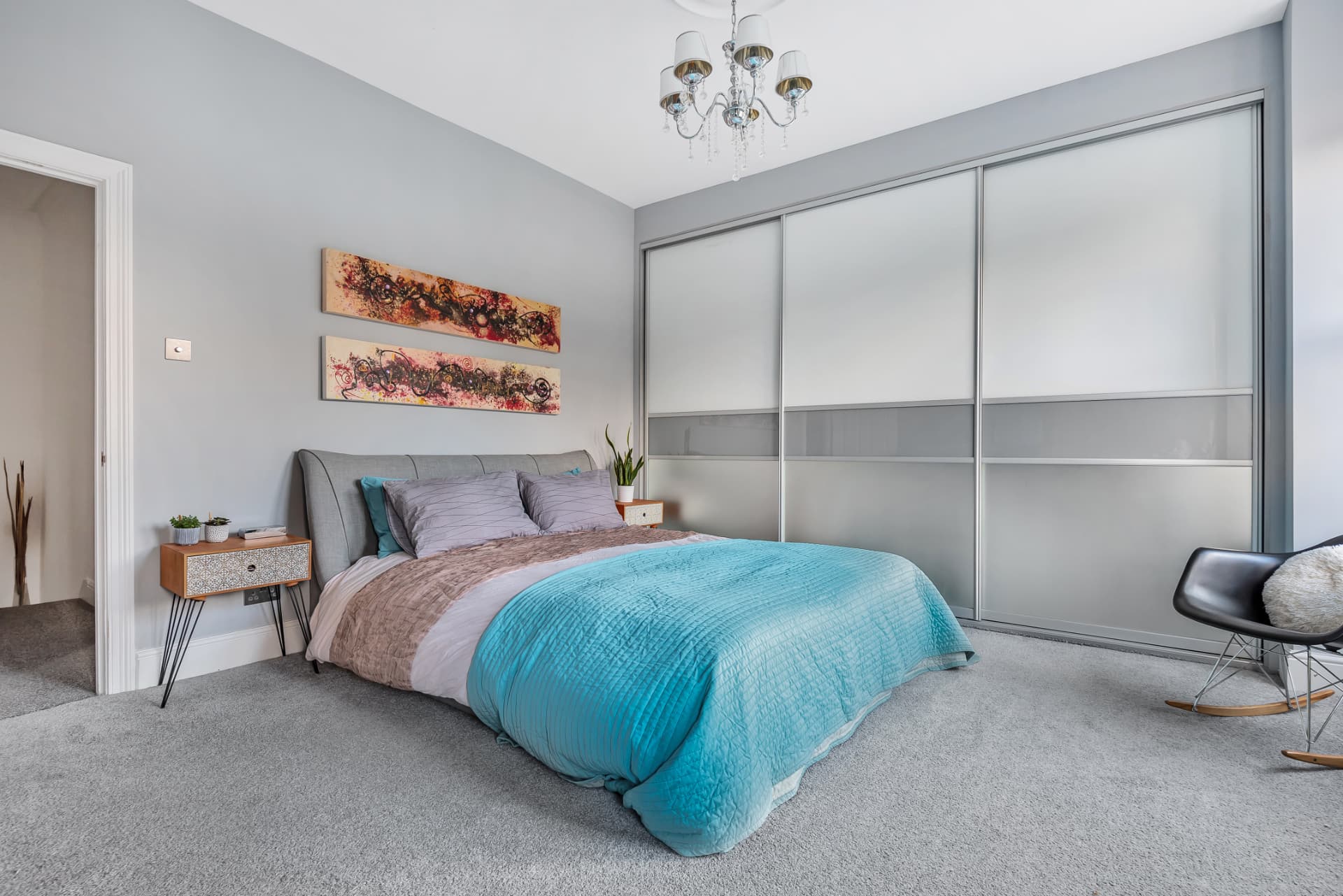 Main bedroom with grey sliding wardrobes, teal bedspread and abstract artwork