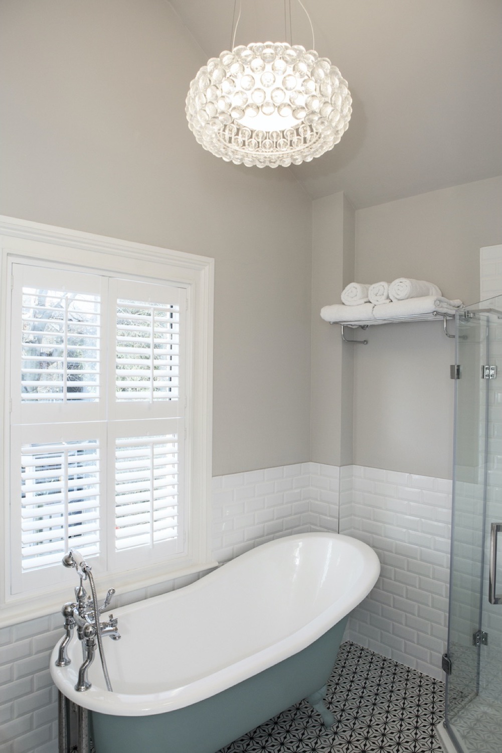 Duck-egg roll-top bath beneath a crystal bubble pendant and shuttered window