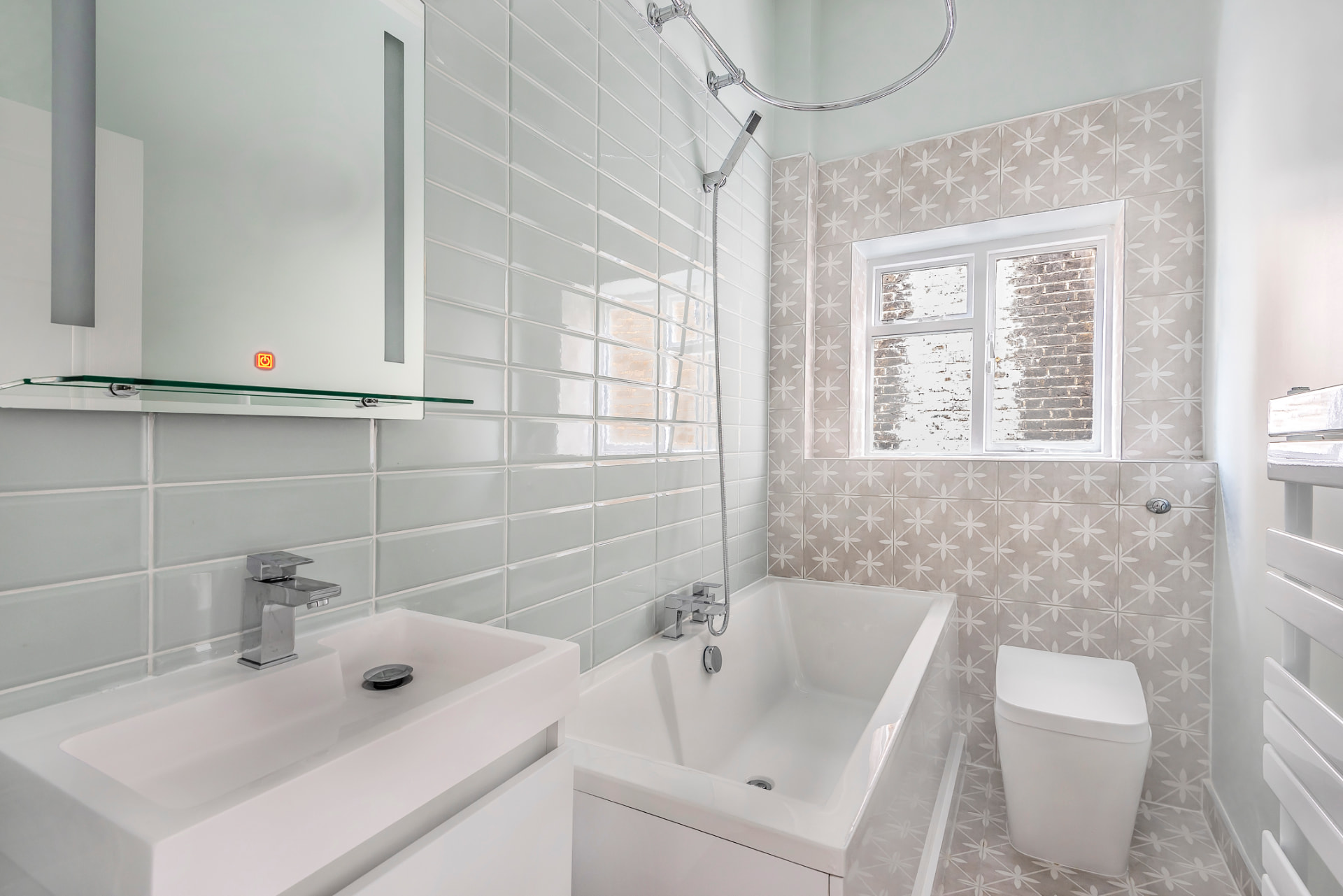 Bathroom with grey metro tiles, patterned feature wall, bath with shower and floating basin