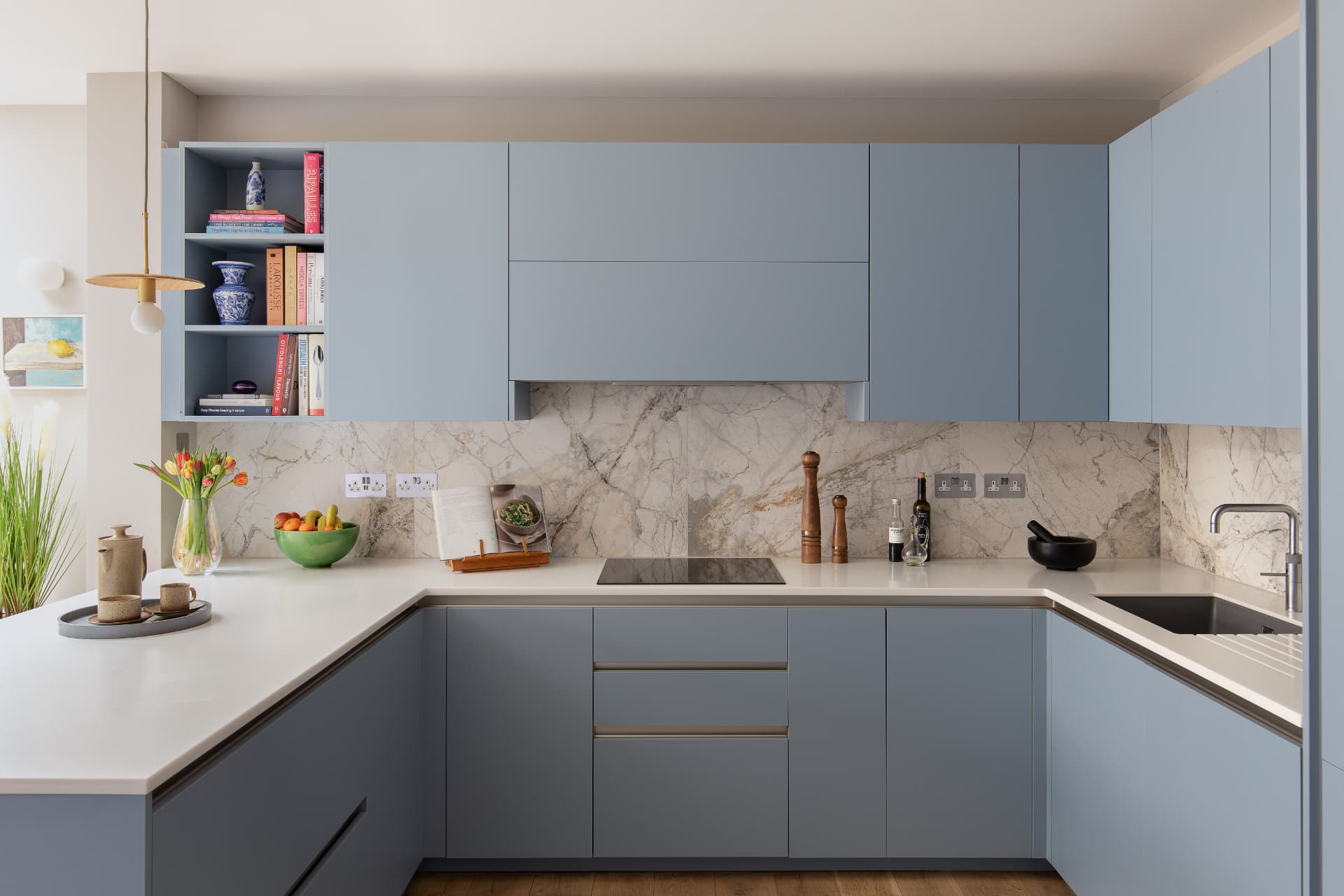 U-shaped pale blue handleless kitchen with white worktops and marble-effect splashback