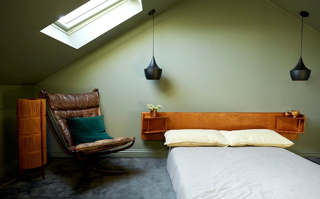 Loft bedroom under the roof window with leather lounge chair and teak headboard