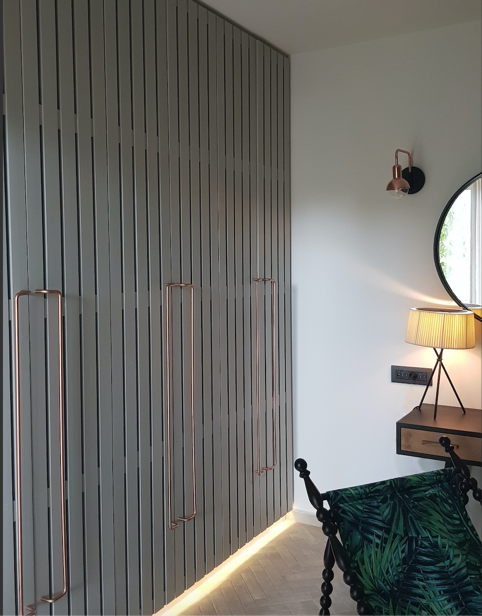 Floor-to-ceiling bespoke wardrobes in a Battersea bedroom with extra-long copper handles and plinth lighting