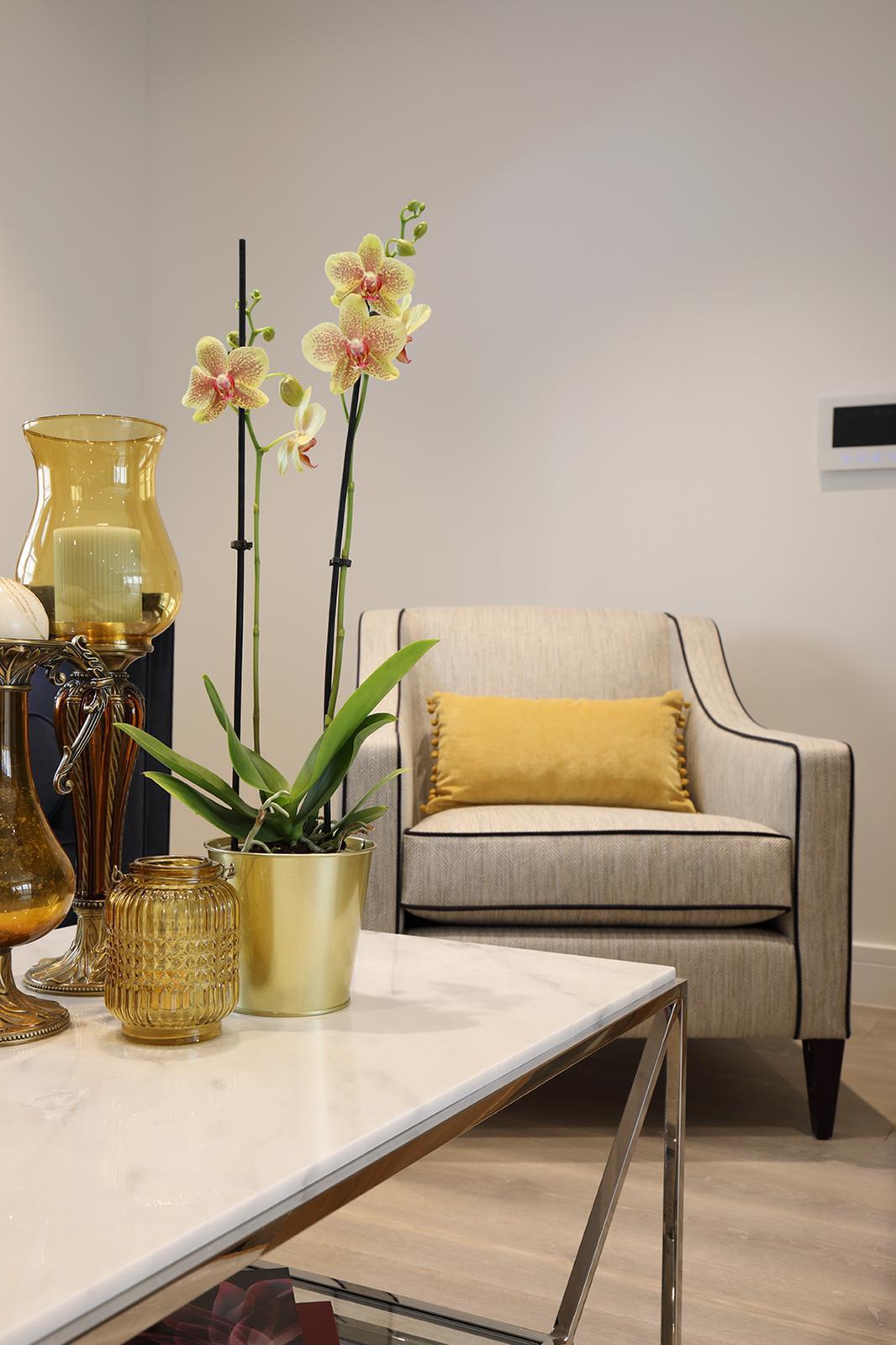 Cream armchair with mustard cushion beside a marble coffee table with orchids and gold glassware