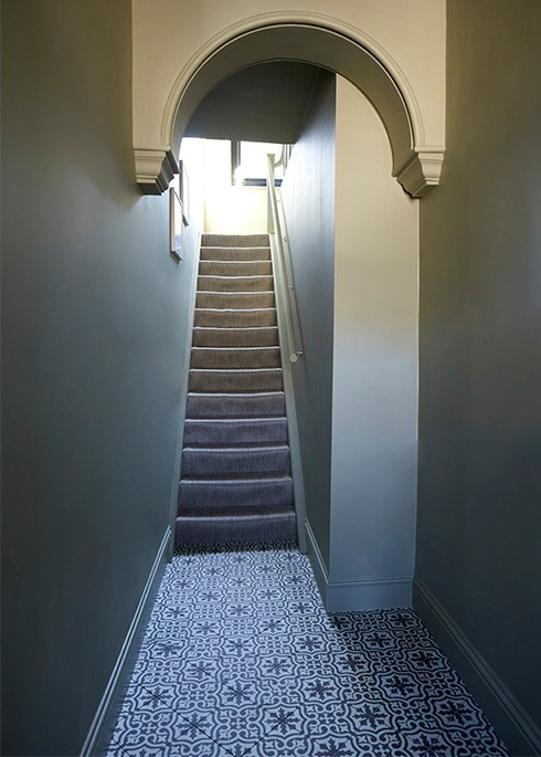Narrow hallway with arched opening, grey stair runner and patterned floor tiles