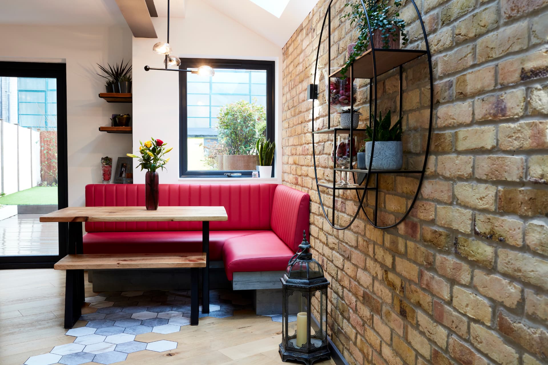 Red leather corner banquette and dining table beside the exposed brick wall