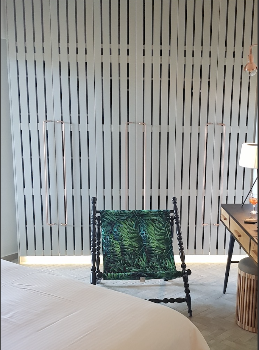 Full-width fitted wardrobes behind a botanical-print chair and writing desk