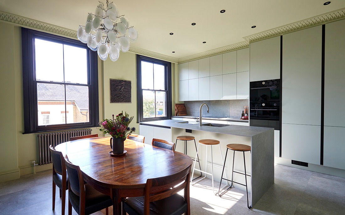 Open-plan kitchen diner with pale handleless kitchen, stone island and round teak dining table