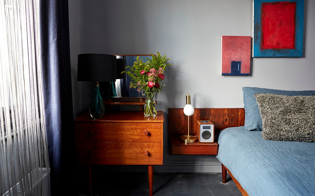 Bedroom with teak bedside cabinet, flowers and contemporary artwork above a blue bed