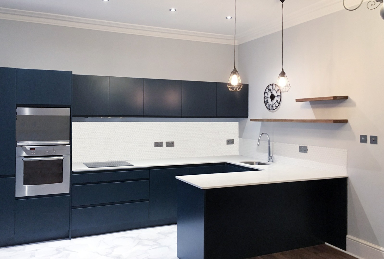 Navy handleless kitchen with white peninsula, open shelves and copper pendant lights in an Honor Oak Park flat