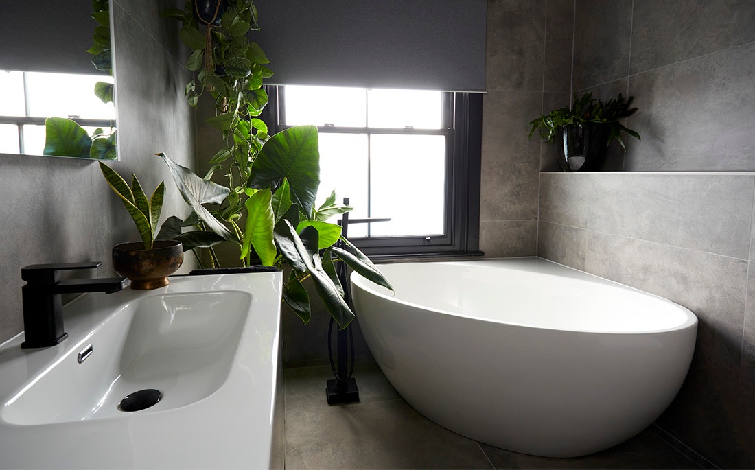 Family bathroom with freestanding bath, large-format grey tiles and tropical plants