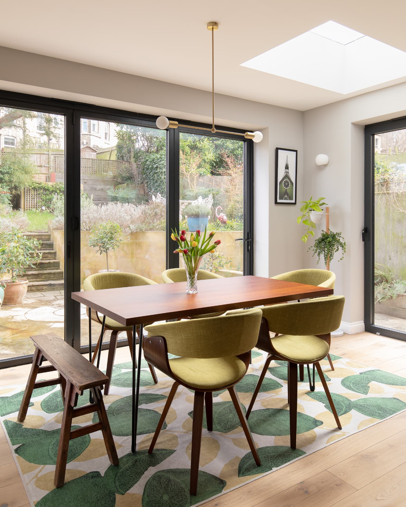 Dining area with walnut table, green upholstered chairs and roof light, looking out to the garden