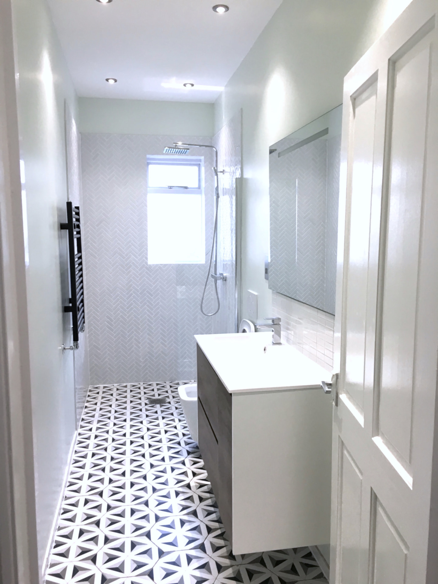 Finished bathroom with walk-in shower, white floating vanity and black and white geometric floor tiles