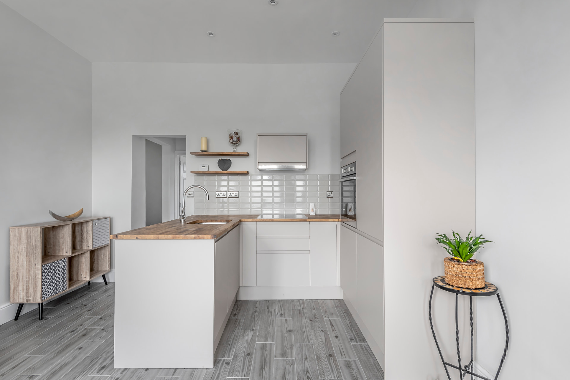Kitchen island with oak top and white units, with open shelving above the hob