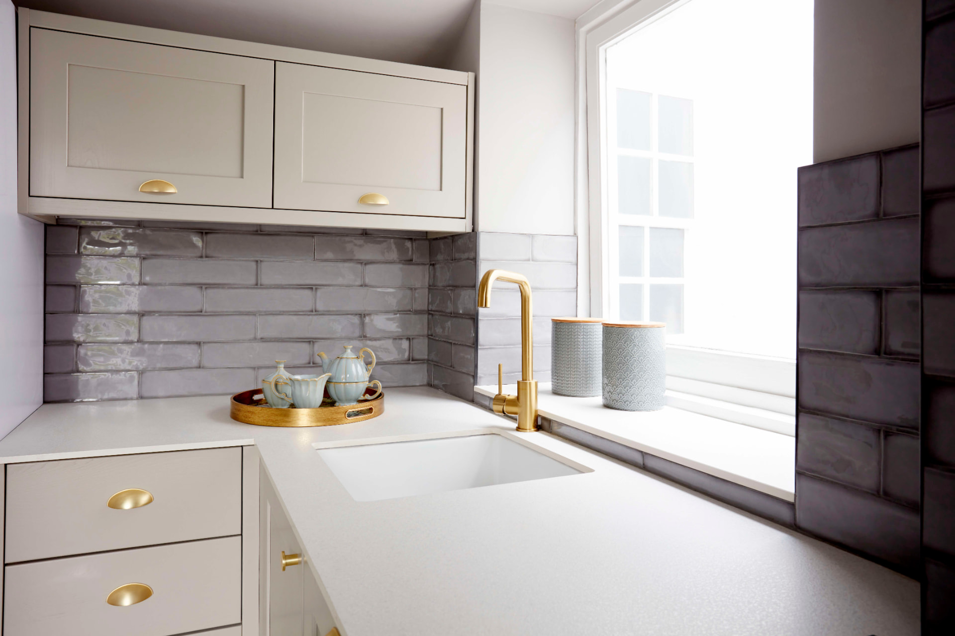 Kitchen sink corner with brass tap, glazed brick splashback and white worktop