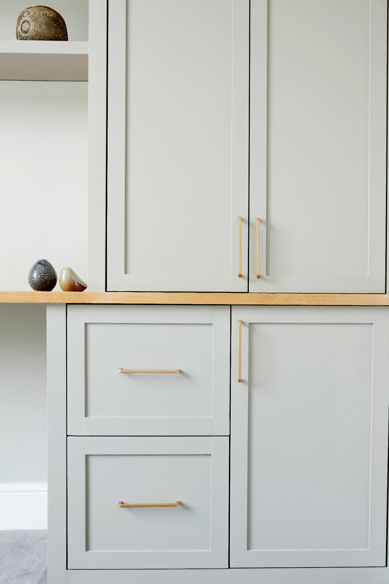 Detail of shaker wardrobe doors and drawers with brass bar handles and oak desk top